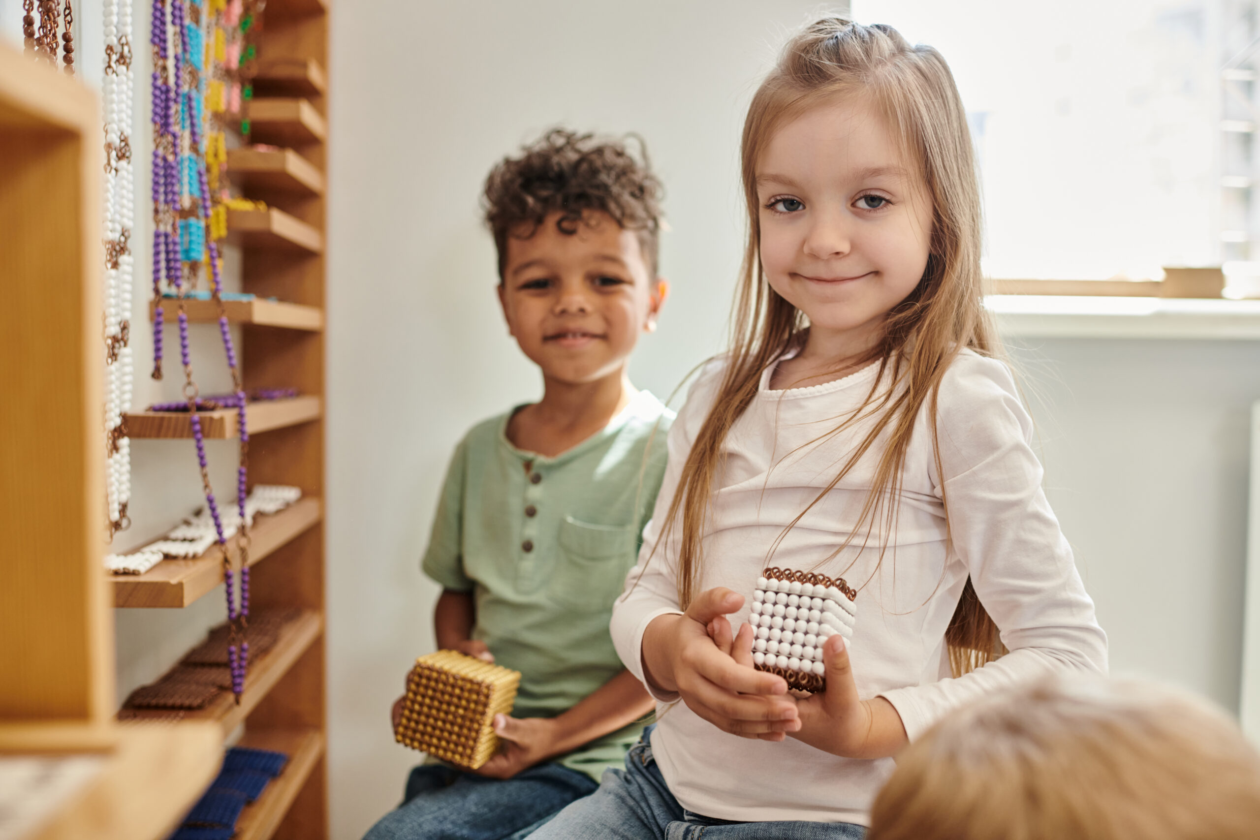 cheerful girl holding cube with beads near african american boy, diversity, Montessori school