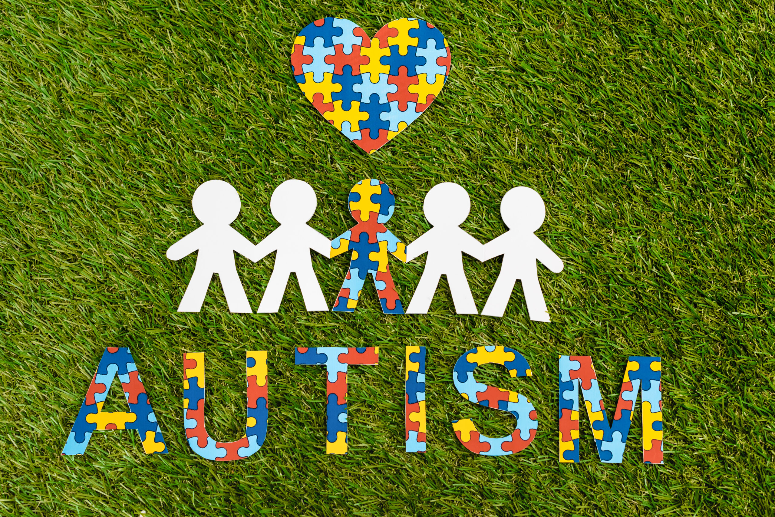 Top view of autism puzzle lettering, decorative heart and special kid among another on green